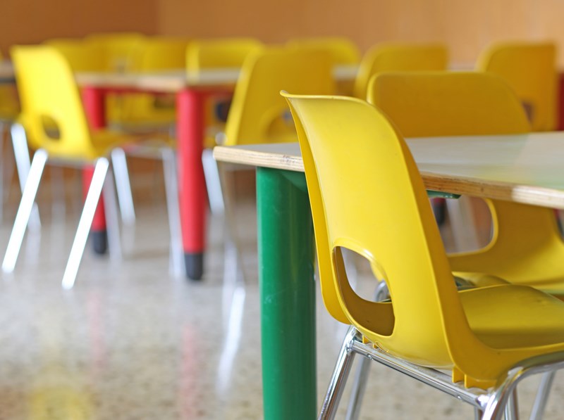 Bilde fra et tomt klasserom, med små møbler ment for barn. Små gule stoler og små bord med røde og grønne ben.